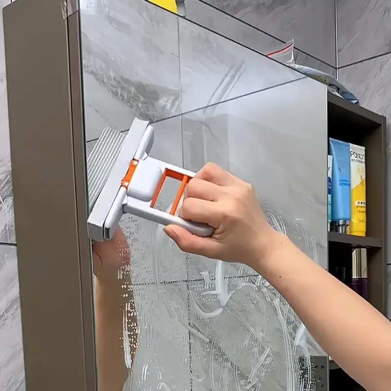 Hand using mini mop to wipe water from a bathroom mirror or glass surface.

