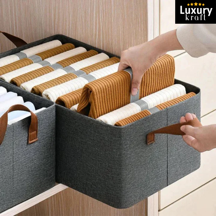Gray storage bins with brown handles containing folded clothes, branded 'Luxury Kraft'.